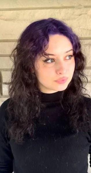 Woman with long black loose waves and a subtle deep-violet wash across the crown roots.