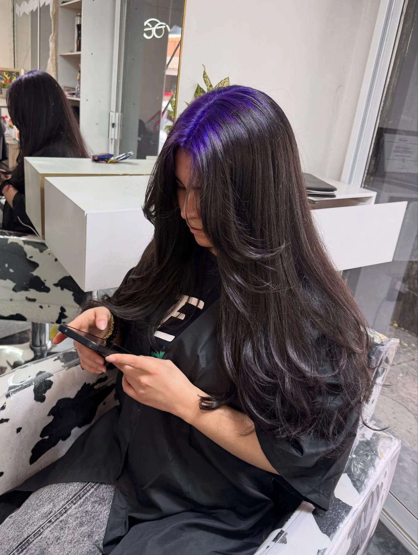 Woman with a very long black layered blowout and vivid violet roots concentrated on one side of the part.