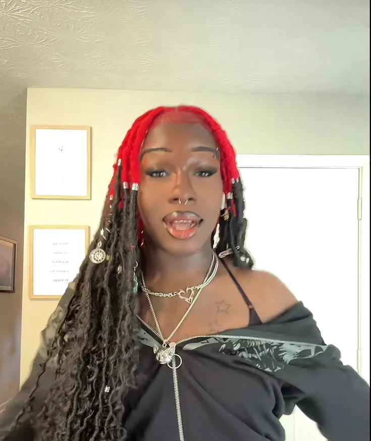 Woman with long dark locs and vivid crimson-red color concentrated around the scalp and crown.