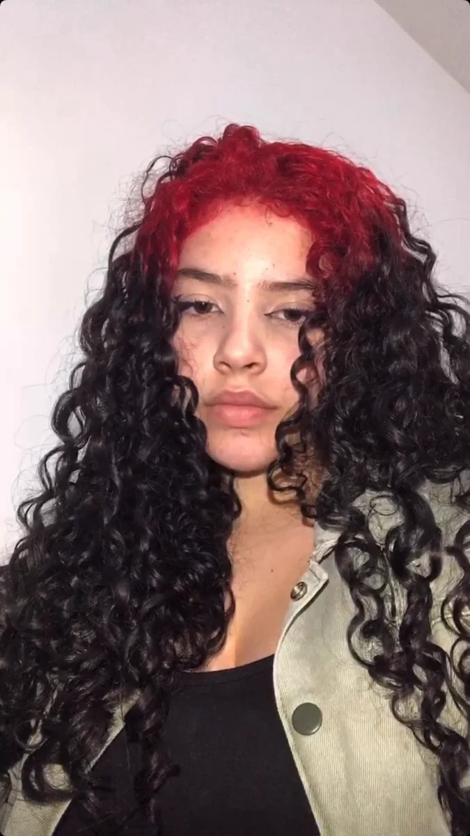 Woman with long black curls and crimson-red ghost roots spread through the visible crown curls.