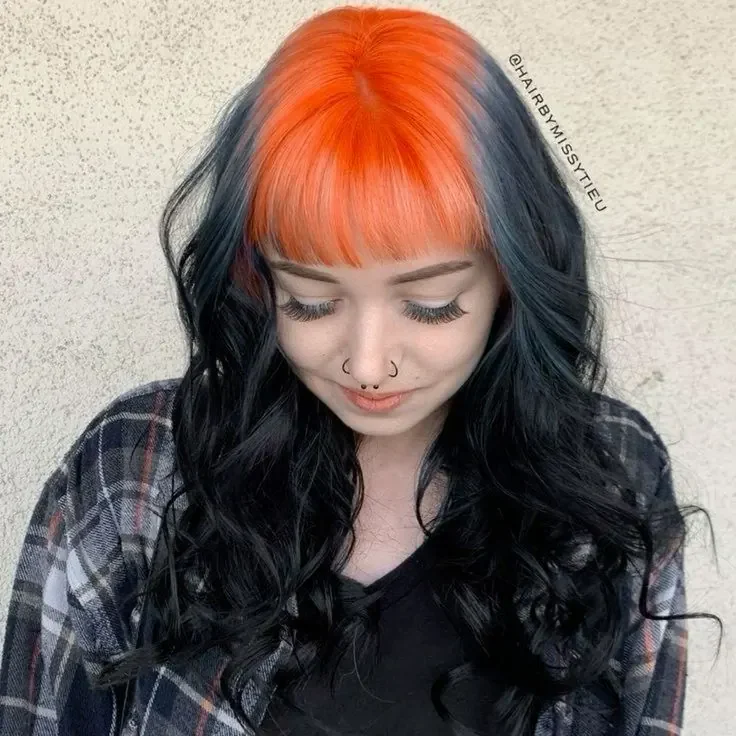 Woman with medium black curly waves and bright orange-copper color covering the front crown and fringe roots.