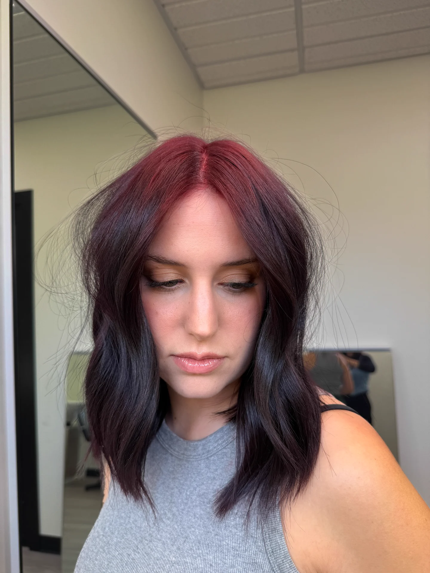 Woman with medium dark brown waves and burgundy-wine red across the full crown and center-part roots.