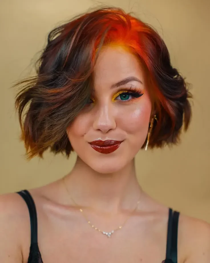 Woman with a short auburn-brown wavy bob and copper-orange root color around the front hairline.