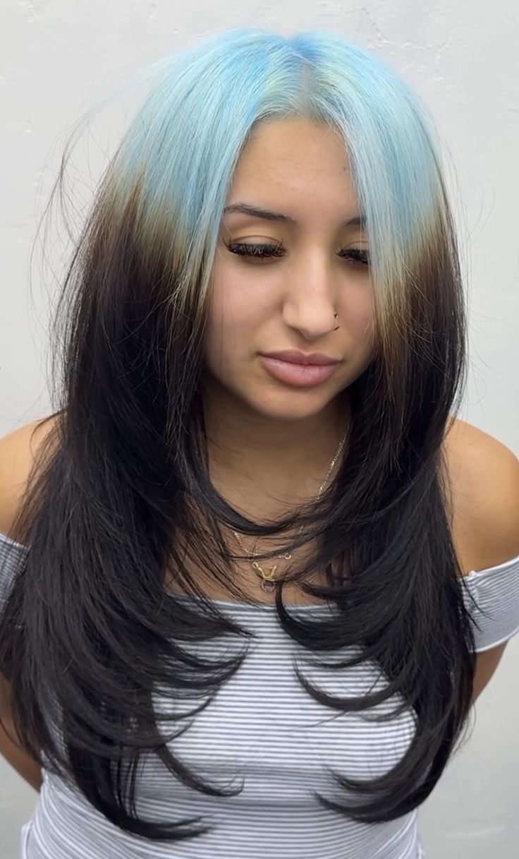 Long layered black hair with pastel blue ghost roots and flipped ends.