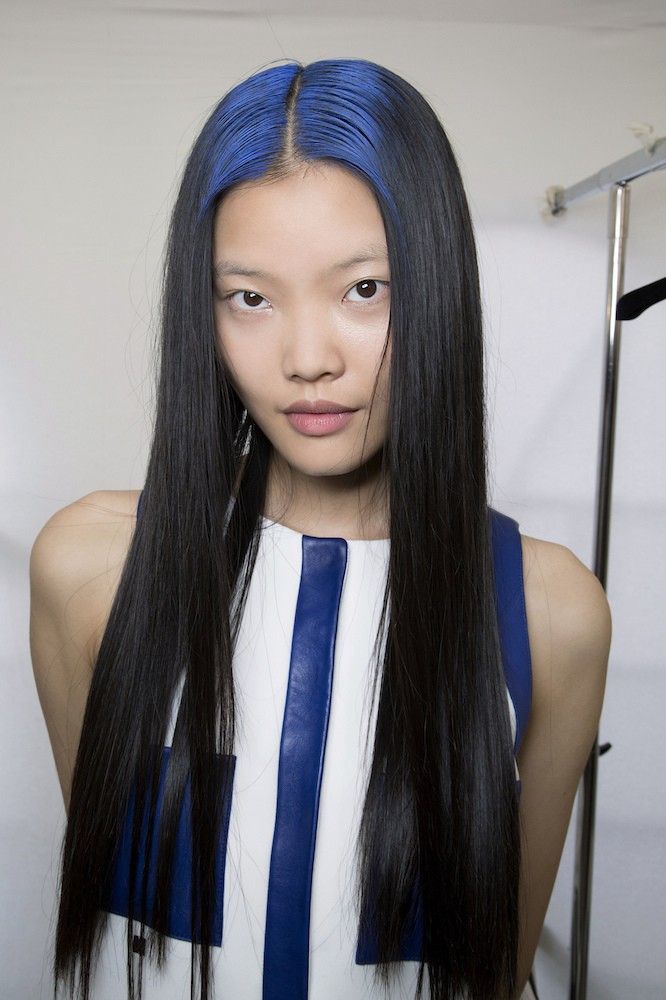 Long pin-straight black hair with cobalt blue ghost roots and a clean center part.