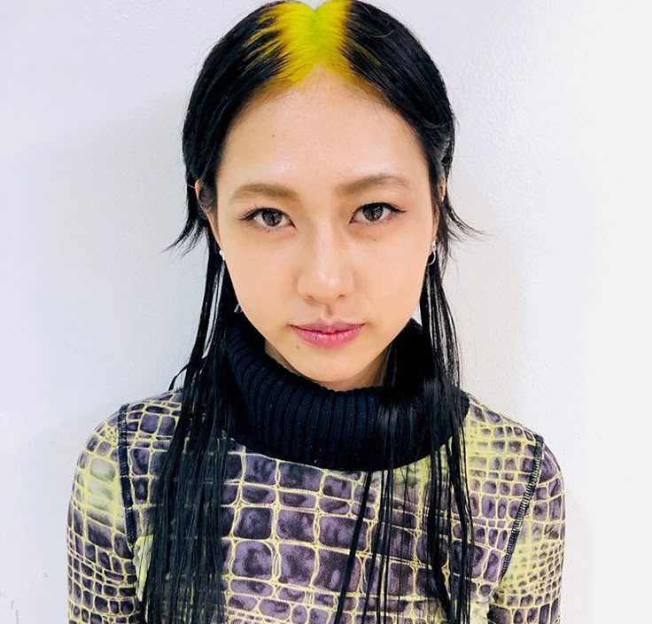 Straight black hair with neon yellow ghost roots and a sharp center part.