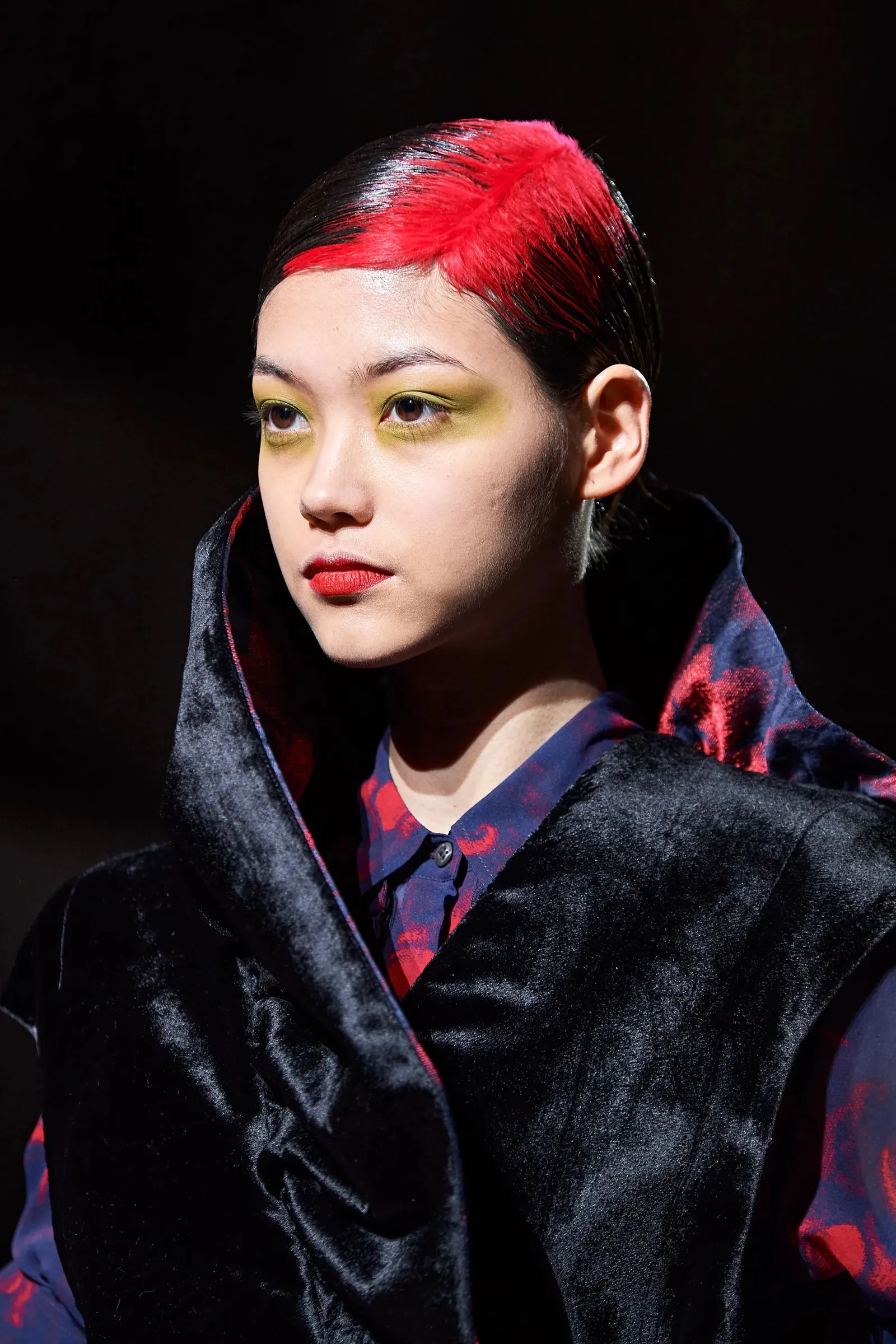 Slick black hair with a vivid red ghost-root panel and a sharp side part.