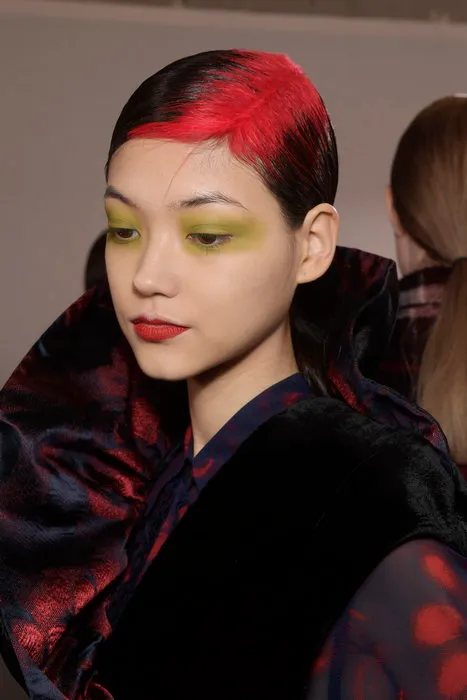 Lacquered black hair with a bright red ghost-root section and sleek side part.