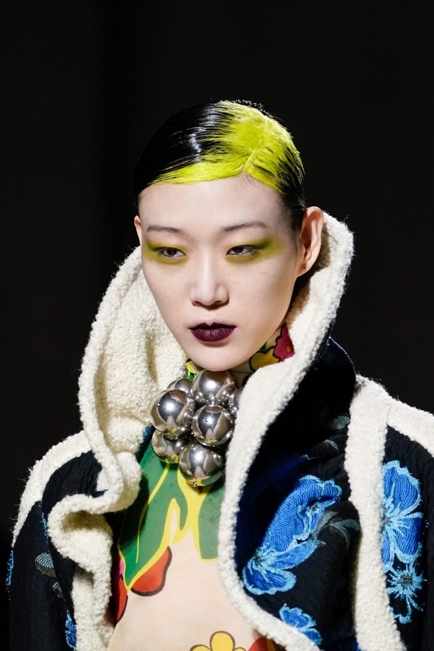 Slick black hair with an acid yellow-green ghost-root flash at the center part.