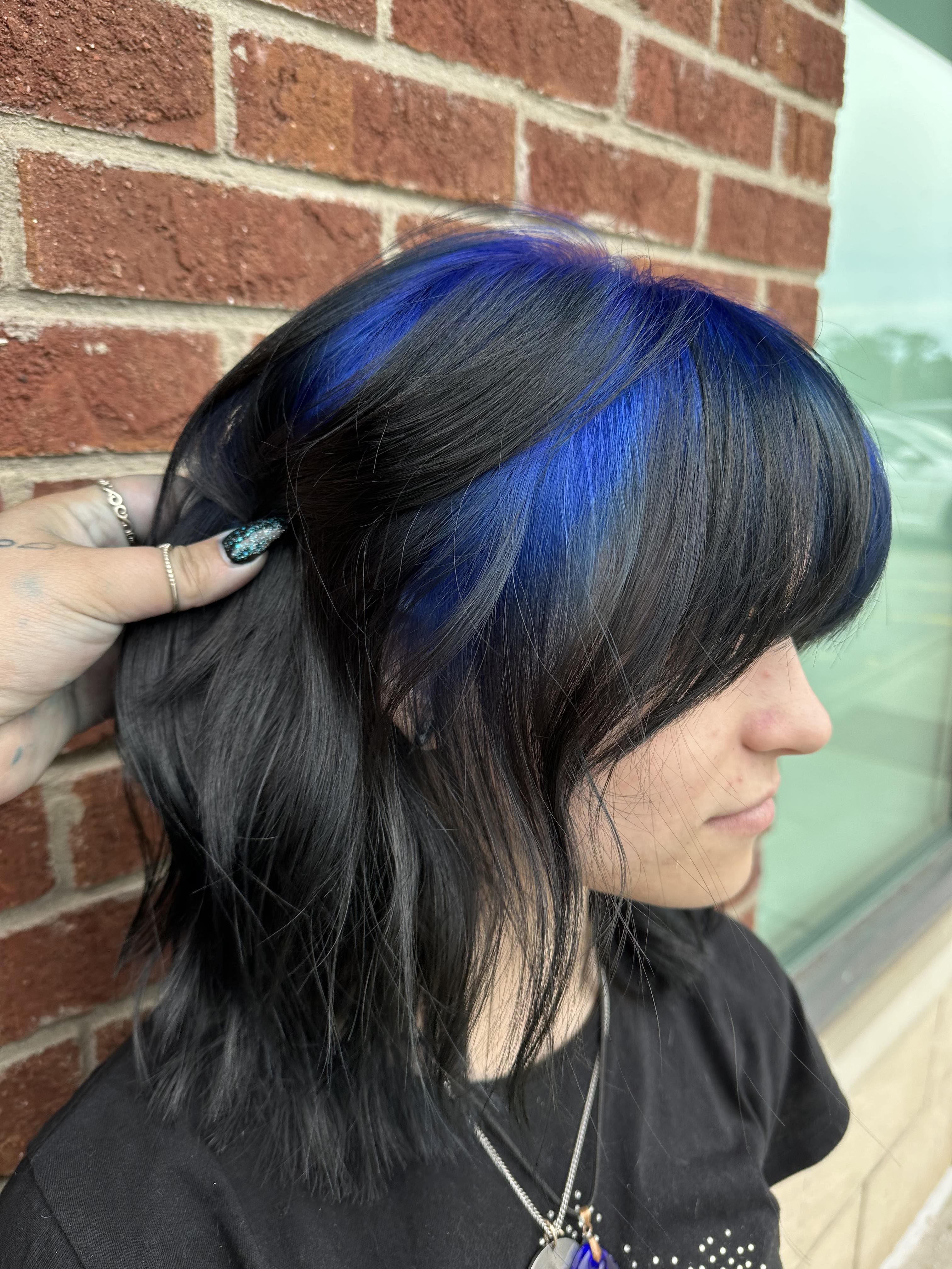 Black shoulder-length hair with electric blue ghost-root panels and blunt bangs.