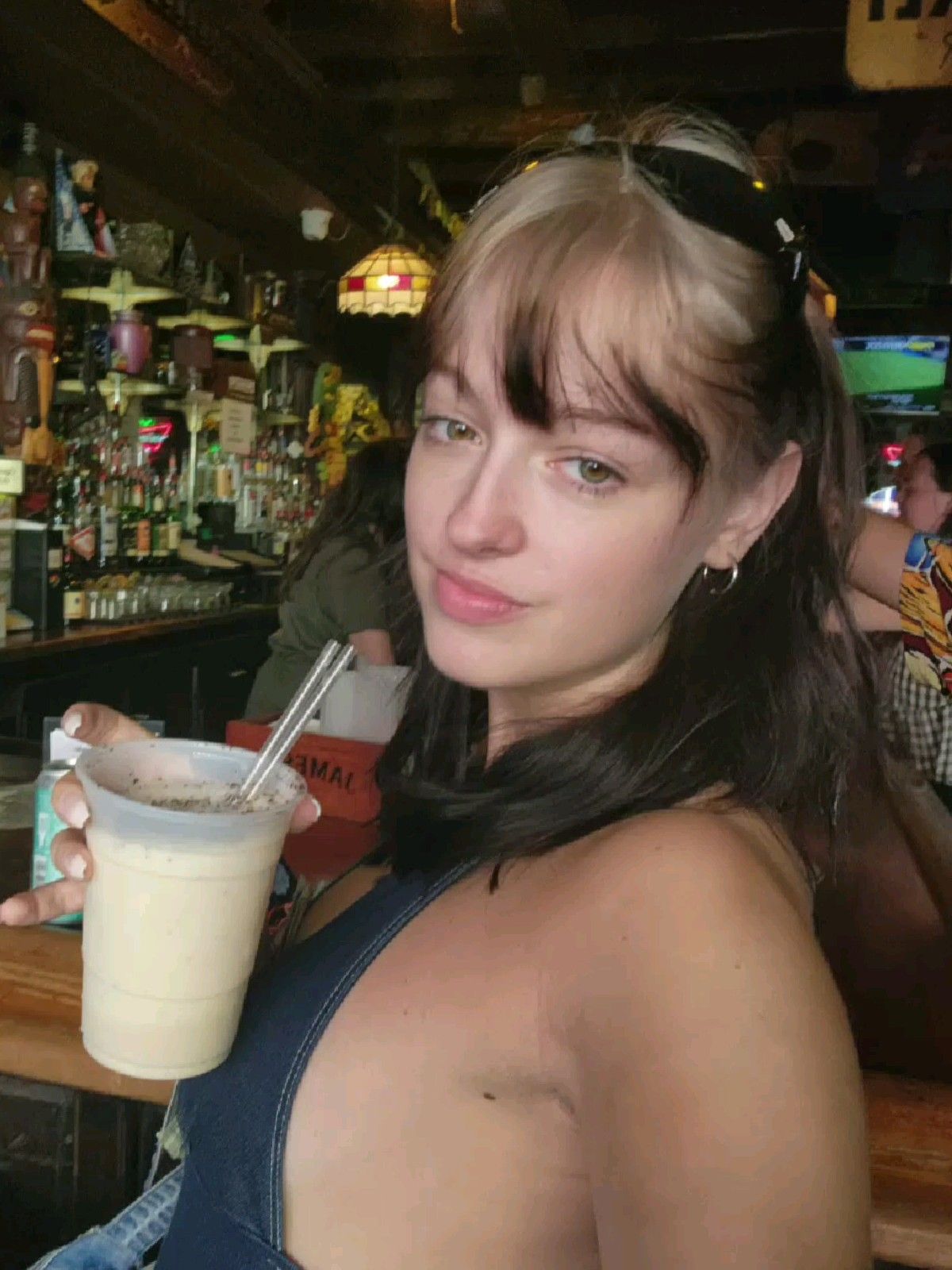 Black shoulder-length hair with platinum ghost roots, wispy bangs, and clipped-back sides.