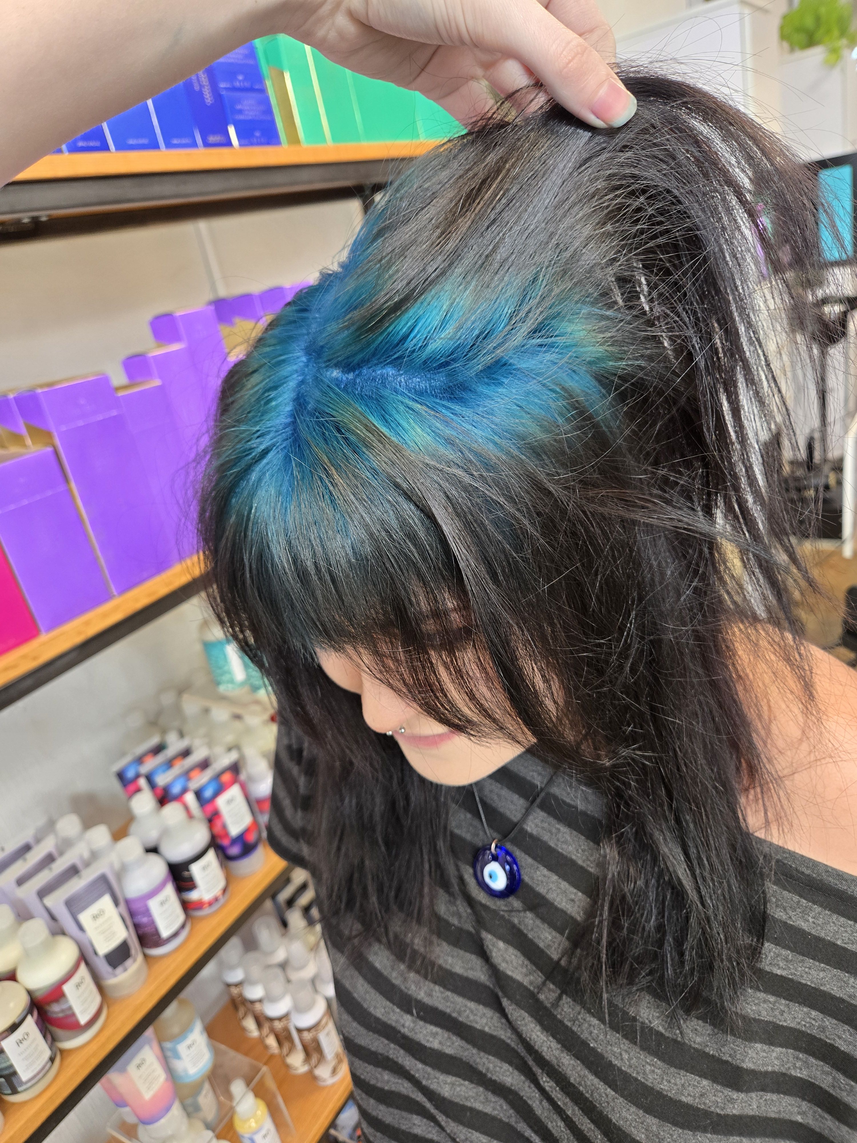 Black shaggy cut with teal-blue ghost roots revealed through the crown.