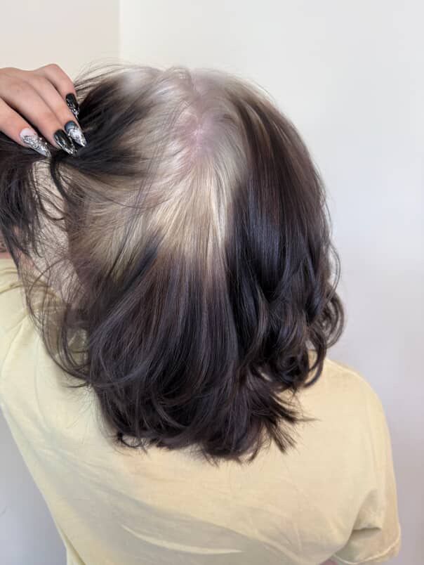 Dark shoulder-length hair lifted to reveal a platinum blonde ghost-root underlayer.