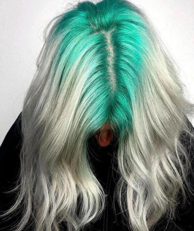 White blonde waves with vivid aqua ghost roots through a center part.