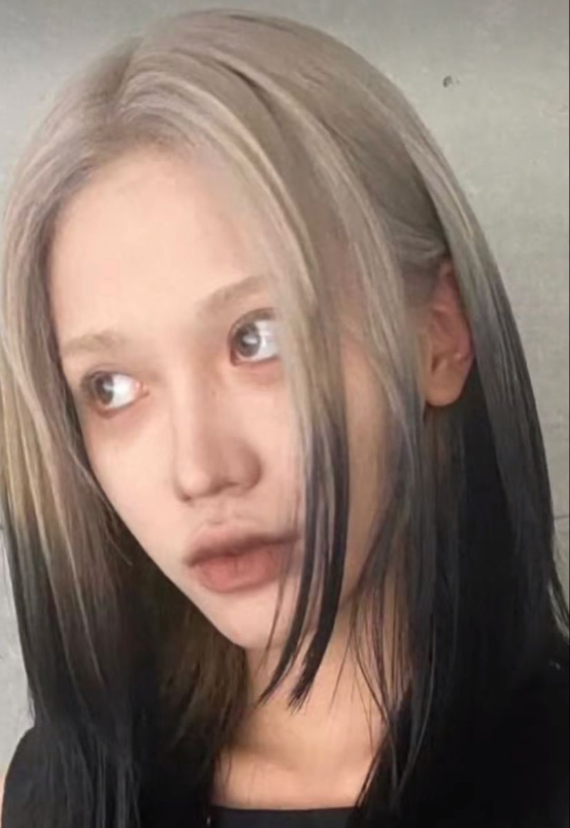 Straight black hair with cool mushroom-blonde ghost roots framing the center part.