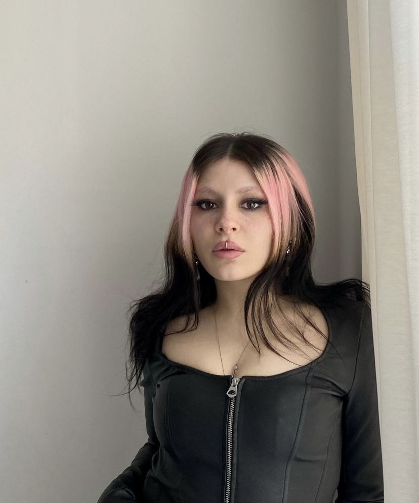 Black hair with pale pink ghost roots and long face-framing pieces.