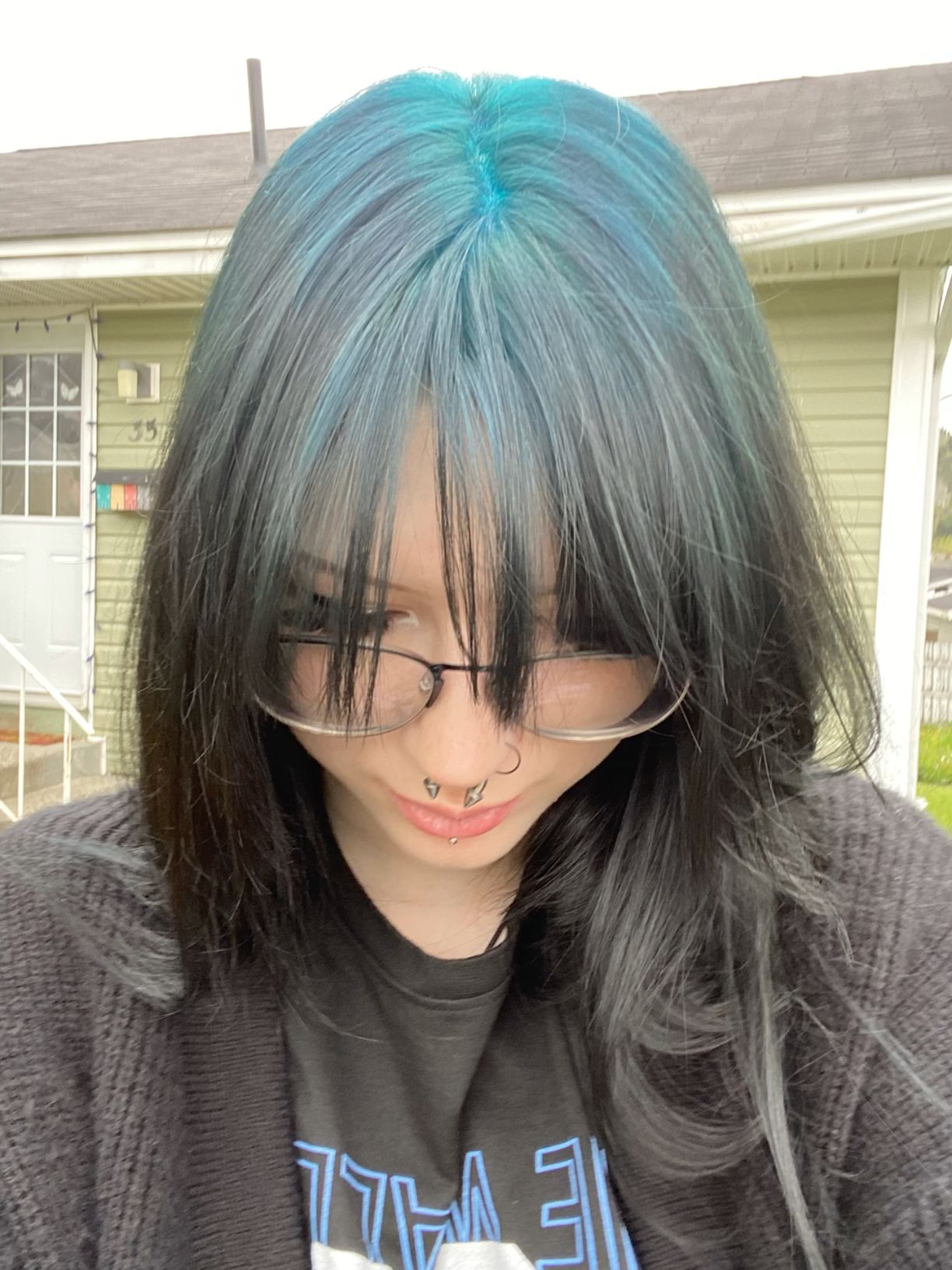 Dark layered hair with teal blue ghost roots through the center part and curtain fringe.