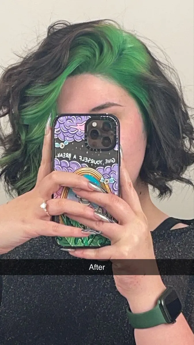 Short black wavy bob with vivid emerald green ghost roots and a side part.