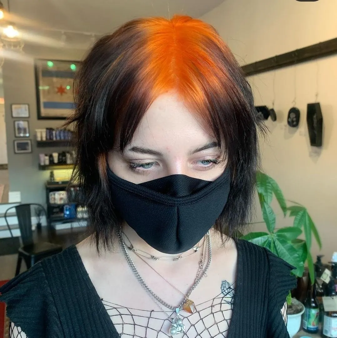 Short black shag with bright orange ghost roots and wispy bangs.