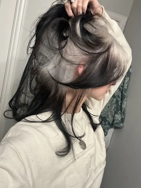 Dark hair lifted to reveal a silver blonde ghost-roots underlayer.