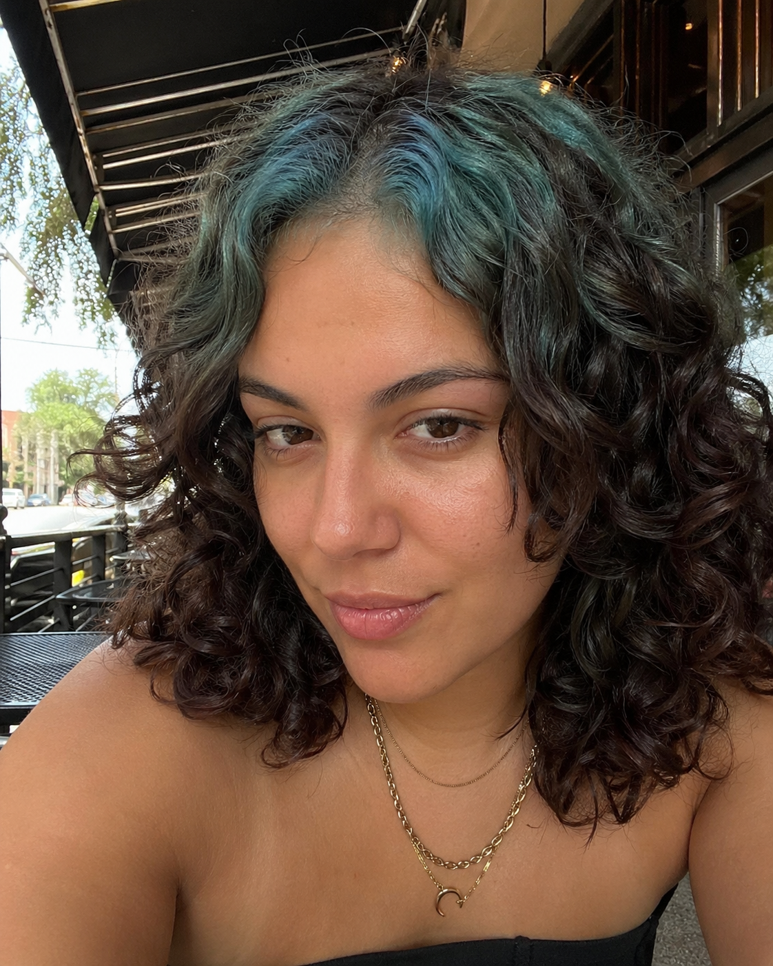 Medium black curly bob with teal-green ghost roots around the face frame.